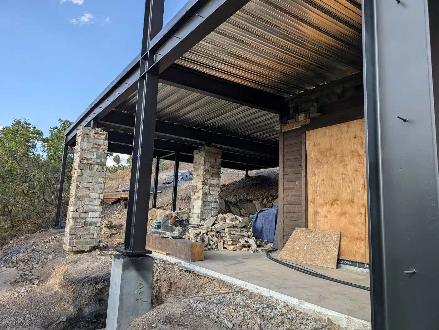 Covered structure on masonry piers — Steel framing bearing on stone-clad piers over an open outdoor area, with the load path carried down through the piers to footings